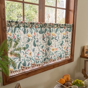 Detail of floral print café curtain with white pom-pom fringe on a wooden window frame