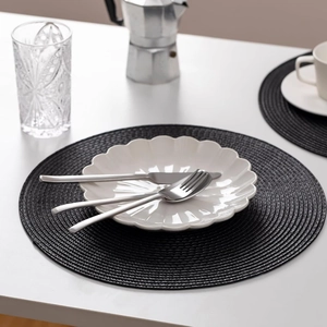 Detail of round black woven placemat with white ceramic plate and metal cutlery on top