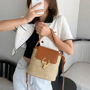 Detail of woven straw bucket bag with brown faux leather trim and round gold buckle