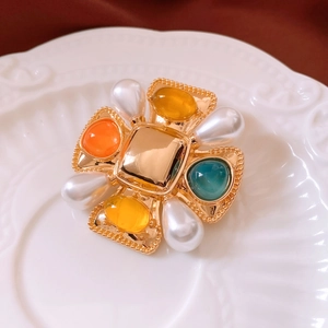 Macro detail of vintage cross brooch with colorful gemstones and pearls on ceramic tray