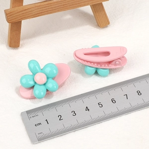 Pair of sweet flower hair clips for girls in pink and turquoise on a soft fabric backdrop