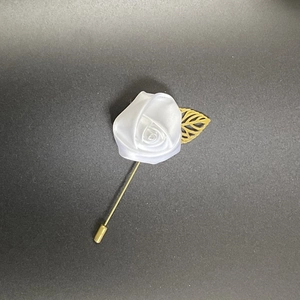 Detail of white fabric rose boutonniere with golden hollow leaf and long metal pin