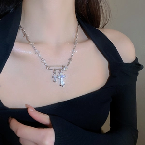 Detailed close-up of a silver safety pin necklace with zircon studded cross pendants on neck