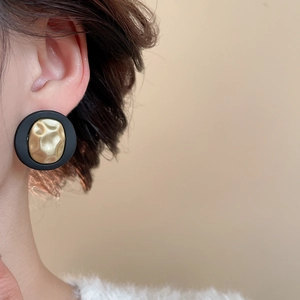 Close-up of retro black and gold round earrings with hammered metal texture on ear
