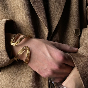 Close-up of golden multi-layer cuff bracelet with high-polish finish on a brown blazer sleeve