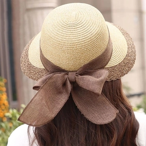 Detail of summer straw hat featuring a dark brown bow knot on a beige woven surface