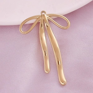 Detailed view of a golden 304 stainless steel bow pendant on a decorative fabric background
