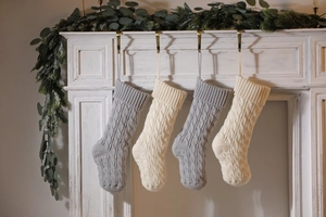 Detail of four knitted Christmas stockings in white and grey hanging on a cozy fireplace