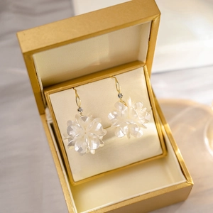Detailed shot of white floral tassel earrings with rhinestones in a gold jewelry box