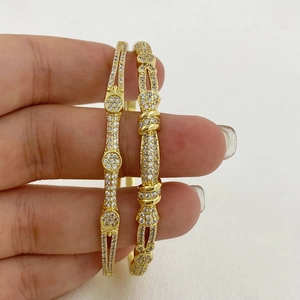 Dettaglio di bracciali dorati con zirconi incastonati tenuti in mano da vicino