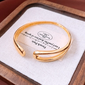 Detail of 18K gold-plated open bangle on a wooden tray with white linen lining