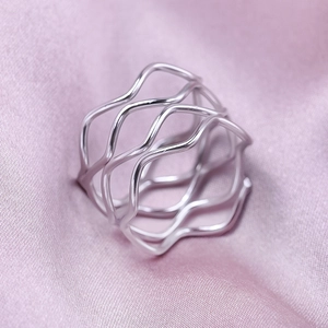 Macro detail of silver wide hollow wavy ring band on soft silk fabric texture