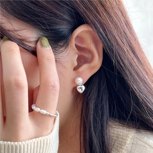 Detail of silver heart charm and pearl earrings on model with a matching ring