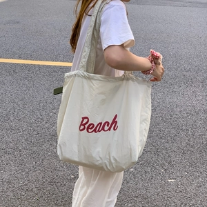 Shoulder shot of a beige drawstring tote bag with red Beach lettering print detail