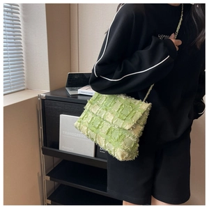 Detail of green woven crossbody bag with fringe edges and golden chain strap