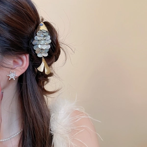 Detail of a gold fish-shaped hair clip with iridescent shell scales and blue eye
