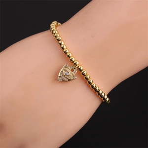 Close-up of gold beaded bracelet featuring a zircon-encrusted heart evil eye charm