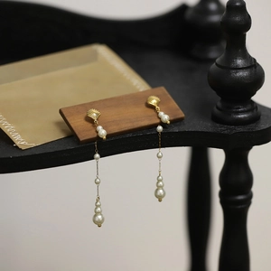 Detail of long pearl tassel earrings with golden shell charms on a wooden stand