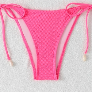 Detail of neon pink bikini bottom featuring textured fabric and side ties with sea shells