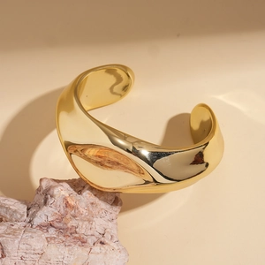 Detailed view of wide gold irregular wave bangle with polished mirror finish on natural rock