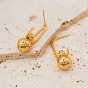 Detailed close-up of gold-plated stainless steel ball drop earrings on beige stone