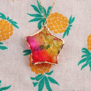 Detailed shot of a colorful star pendant with gold chain on pineapple pattern fabric