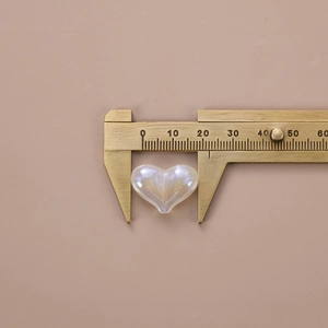 Pearlescent white heart-shaped DIY bead measuring 23mm with a caliper measurement tool