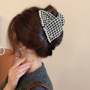 Detail of houndstooth bow hair claw with pearls worn on back of head by model