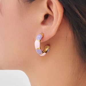 Pastel pink and purple enamel C-shaped hoop earrings with gold trim worn by a model