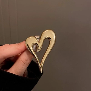 Close-up of a minimalist golden heart-shaped metal brooch with a smooth polished finish