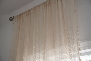 Detailed close-up of beige crochet lace curtain with geometric patterns and tassels