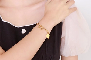 Dettaglio di un bracciale in acciaio al titanio dorato con perline e ciondolo tondo
