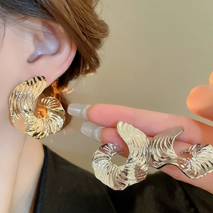 Detailed view of large gold metallic ripple textured earrings on a model in minimalist style