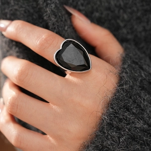 Macro detail of a heart-shaped black gemstone ring on a silver band worn by a model
