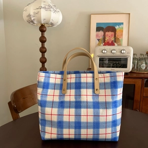 Detailed close-up of blue plaid canvas tote bag with leather straps in a home setting
