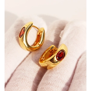 Elegant gold U-shaped hoop earrings with oval red zircon stones held in a gloved hand