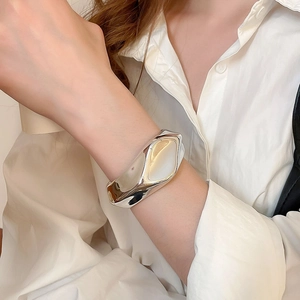 Close-up of a chunky silver irregular open bangle with a polished mirror finish on wrist