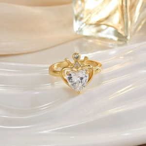 Macro view of a gold heart-shaped gemstone ring with a crown design on white ceramic