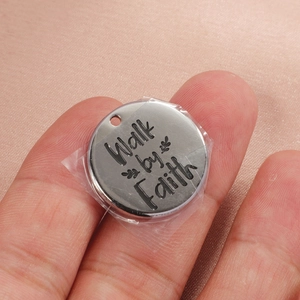 Stainless steel round pendant with Walk by Faith engraving held by hand for size