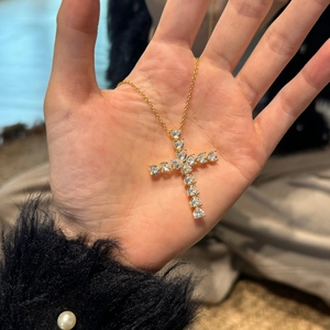 Detailed view of a gold cross pendant necklace with heart-shaped crystals held in hand