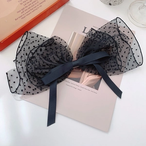 Detailed view of a black polka dot lace bow hair clip with satin ribbons on a book
