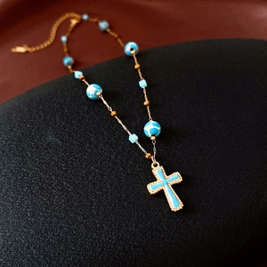 Details der Vintage Goldkreuzkette mit blauen Marmorperlen auf schwarzem Lederhintergrund