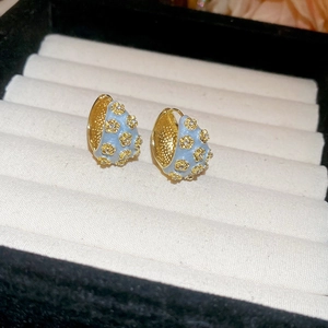 Macro detail of light blue enamel huggie earrings with gold floral zircon accents