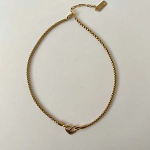 Close-up of golden box chain necklace with a textured heart-shaped clasp detail