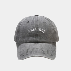 Detailed close-up of white FEELINGS embroidery on washed dark gray cotton baseball cap