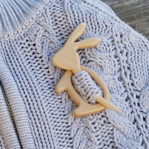 Handcrafted wooden rabbit brooch pin shown on a light blue knitted sweater fabric