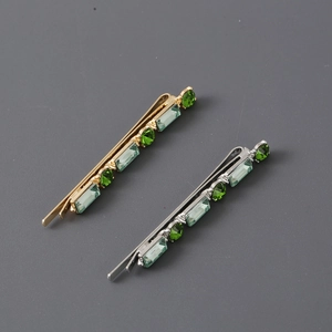 Detail of gold and silver hair clips with green rectangular and round gemstones