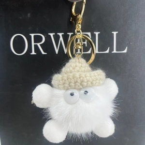 Close-up of white plush monster keychain with big eyes and cream knitted hat details