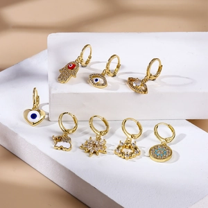 Set of 8 gold piercing earrings with evil eye, hamsa hand and zircon charms on display