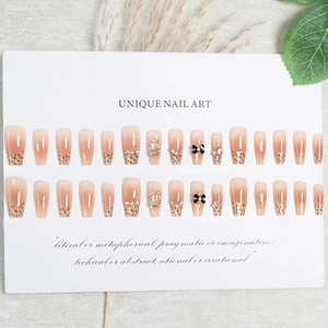 Pink gradient press-on nails with black bows and pearl accents on a white display board